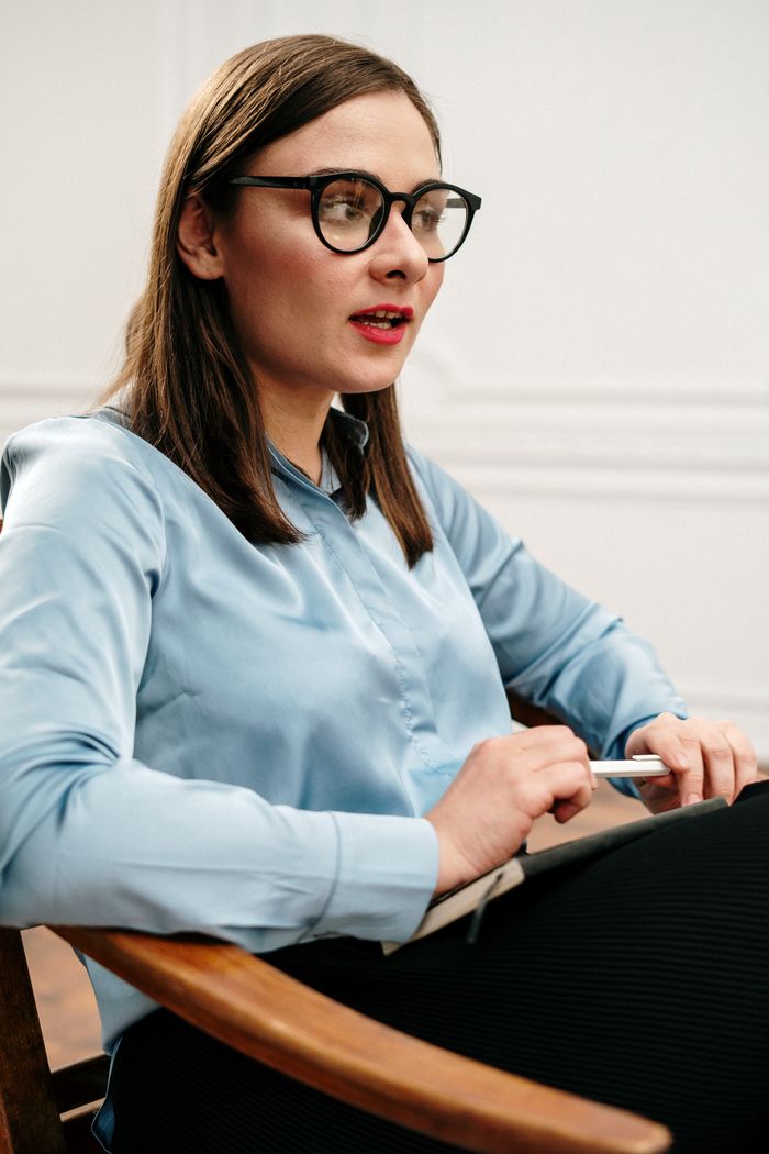 A professional woman in glasses engaging in a thoughtful indoor discussion.
