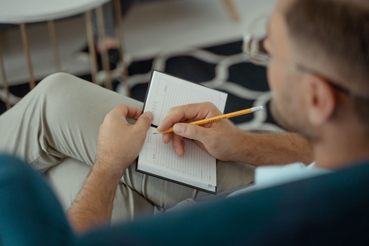 Crafting Captivating Headlines: Your awesome post title goes here An adult man writing with a pencil in a notebook while seated indoors.